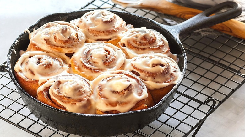 Freshly baked cinnamon rolls with icing in a cast iron skillet over a metal wire rack
