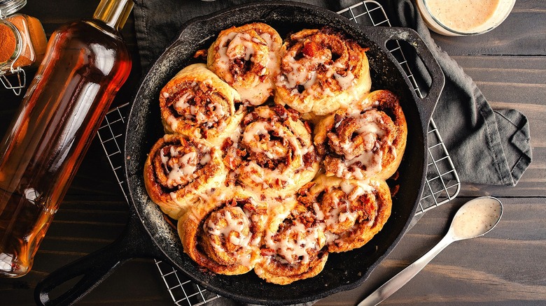 Freshly baked cinnamon rolls covered in crumbled bacon and glaze in a cast iron skillet