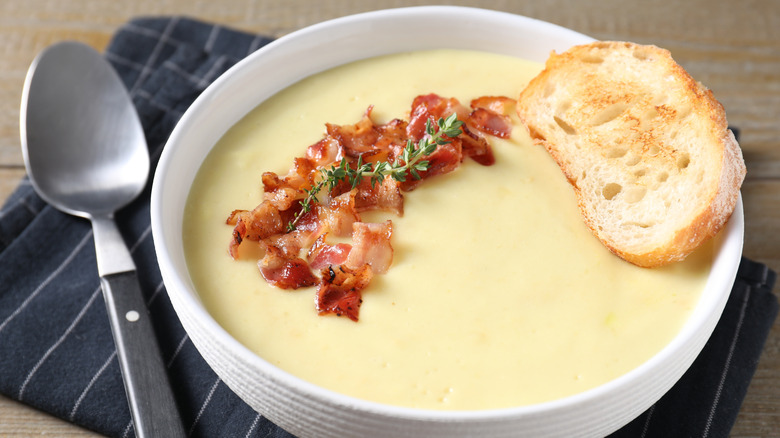 Bowl of baked potato soup topped with bacon, bread, and rosemary