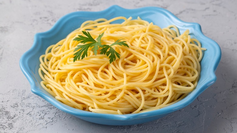 Plain buttered spaghetti with herb garnish in blue bowl