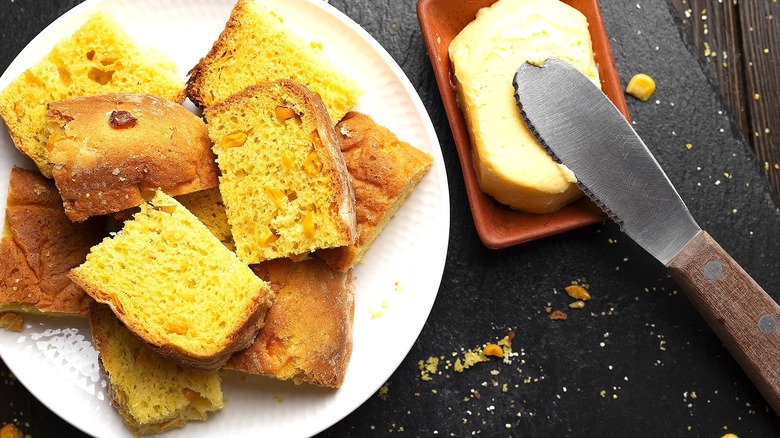 Sliced cornbread on a white plate next to a butter dish filled with softened butter