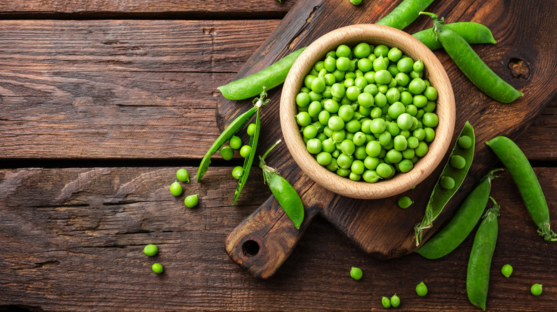 Peas in bowl on a wooden cutting board and table.