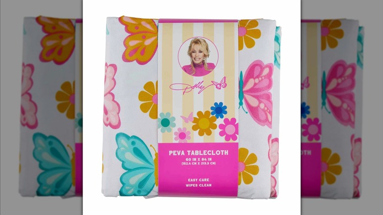Packaged PEVA tablecloth with blue, pink, and gold butterfly decor wrapped with a label with Dolly Parton's headshot and signature