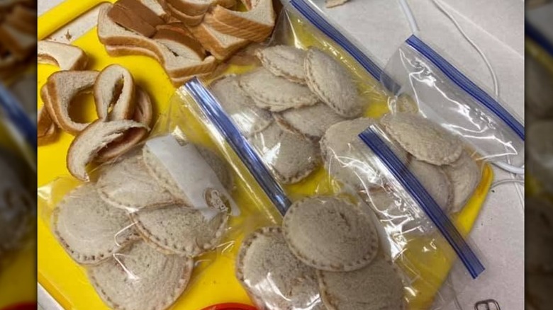 Freezer bags full of homemade Uncrustables next to sandwich crusts on a yellow cutting board.