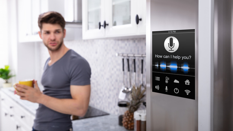A person is seen standing in a kitchen beside a smart refrigerator.
