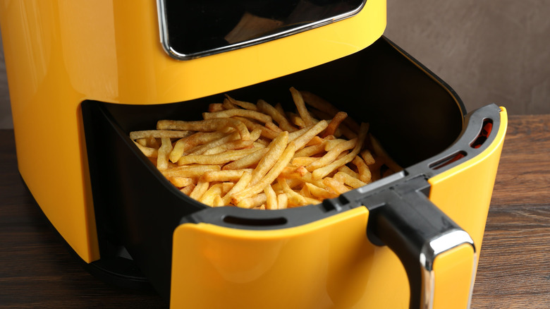 Yellow air fryer with basket partially opened containing french fries inside.