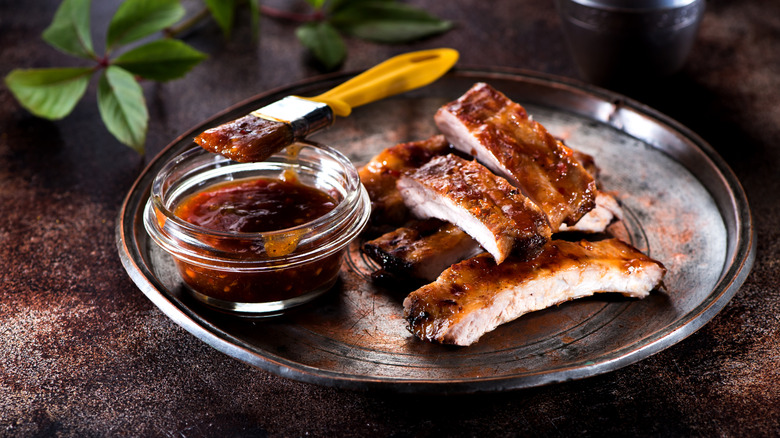 A plate of sliced baby back ribs with a small bowl of sauce and a basting brush.