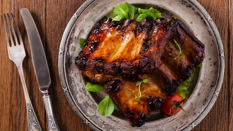 A top view of a plate of baby back ribs, artfully presented with garnish, and a fork and knife on the side.