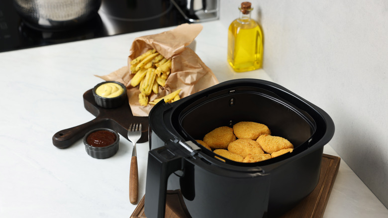 Chicken nuggets in an air fryer with a bottle of oil in the background