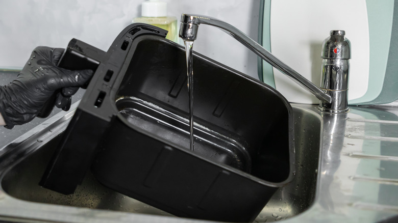 Hands washing an air fryer basket in a kitchen sink.