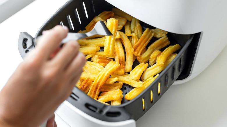Hand removing a french fry with a metal fork from an air fryer basket