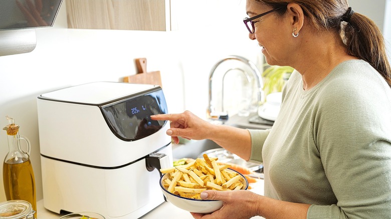 Woman holding a bowl of french fries while preheating an air fryer