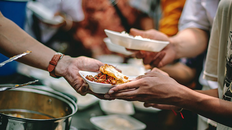 An arm handing out a plate of food.