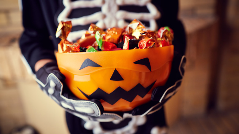 Child in a skeleton Halloween costume holding a pumpkin bowl full of candy