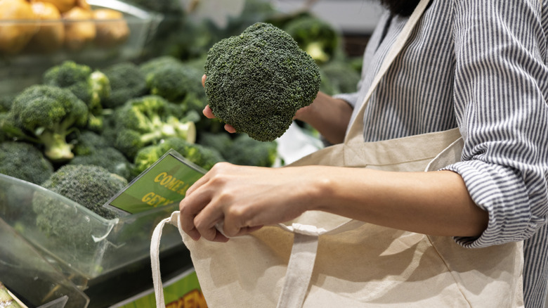 Person putting broccoli into their reusable grocery bag