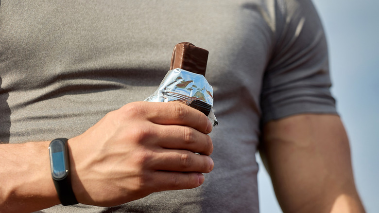 Man wearing a t-shirt and an exercise watch holding a protein bar