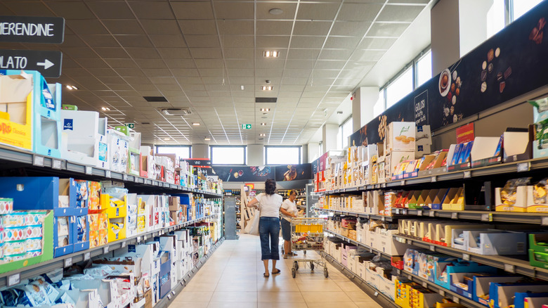 Two women pushing shopping carts and buying groceries inside a brightly lit Aldi store.