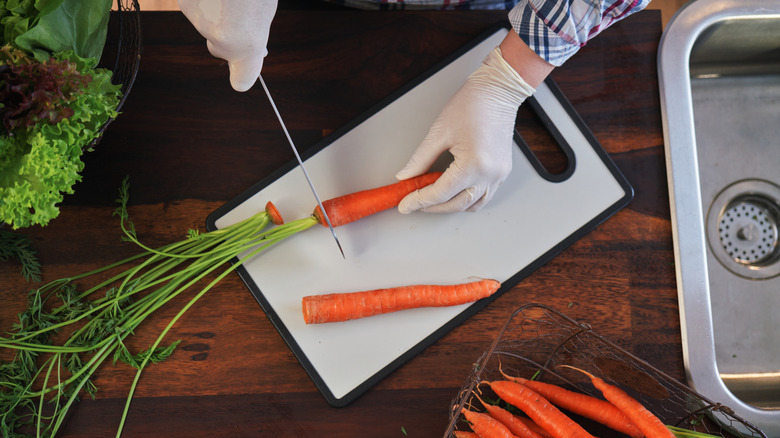 Overhead view of person shopping carrots on a white plastic cutting board