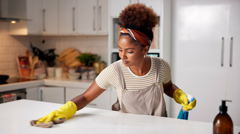 Women wearing overalls, a t-shirt, and yellow cleaning gloves wiping down her kitchen island
