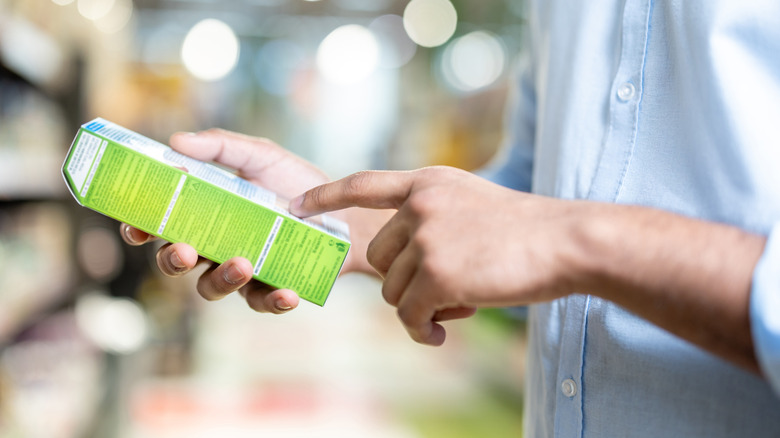 A person's hands are seen holding a grocery item as though to scan its ingredients.