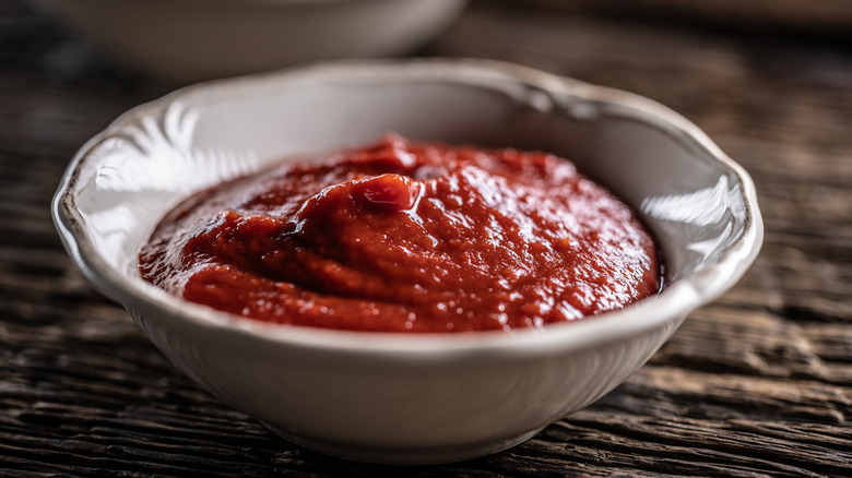 Ketchup is pictured in a white bowl on a wooden table.
