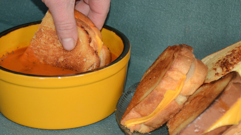Grilled cheese sandwich being dipped in a bowl of tomato soup