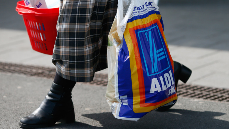 Person carrying basket and Aldi bag full of groceries