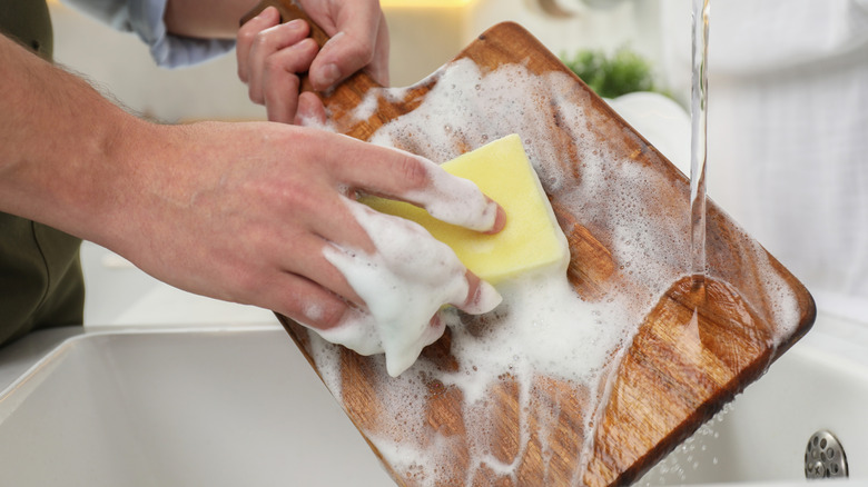 Man washing wooden cutting board in kitchen, closeup
