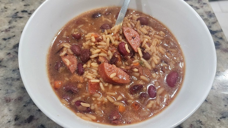 White bowl of red beans and rice with sausage and broth.