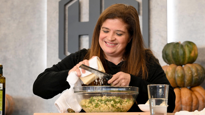 Chef Alex Guarnaschelli smiling and grating cheese into a bowl of pasta