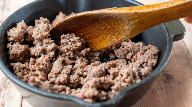 Cooked ground beef in a skillet with a wooden spoon