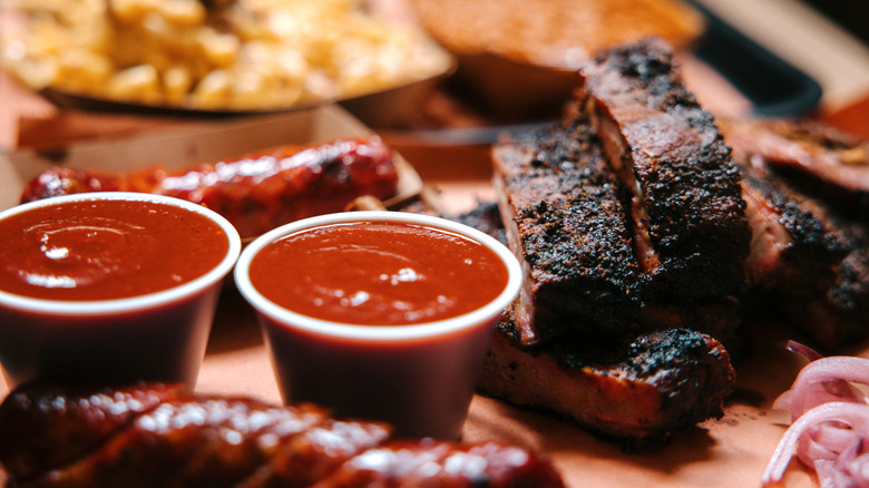 Two containers of barbecue sauce next to cooked ribs