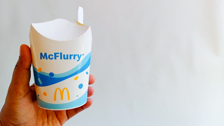 A hand holding a McDonald's McFlurry against white wall