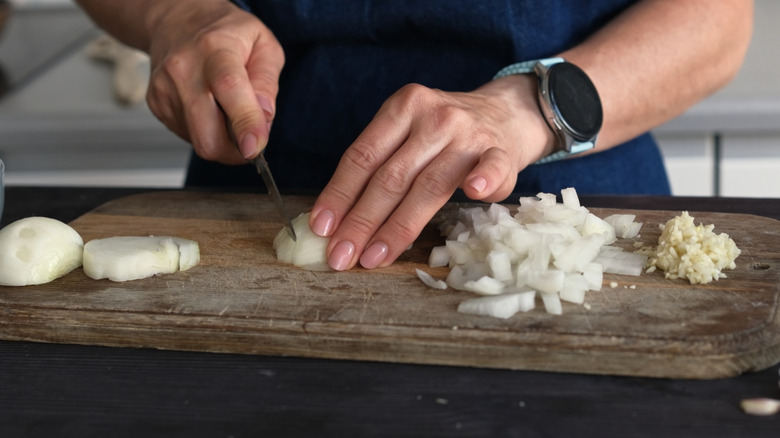 Hands cutting an onion on a cutting board.