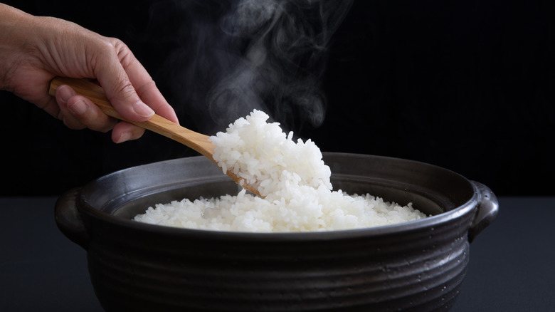Clay pot of steamed white rice with a hand holding a spoon.
