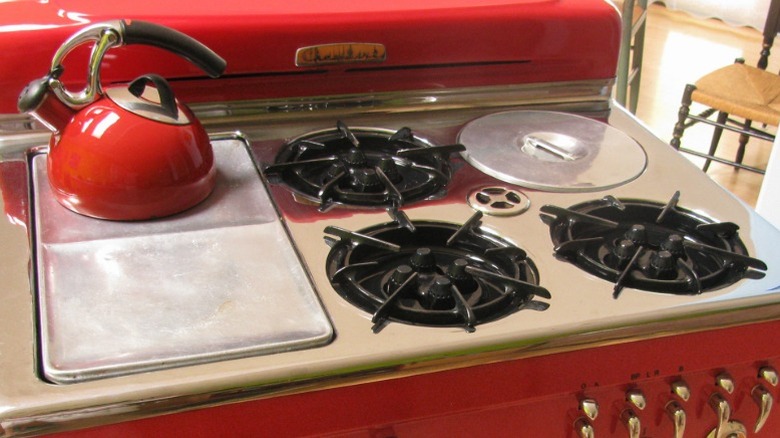 A vintage red oven appliance with a range featuring a deep well cooker burner on the top right.