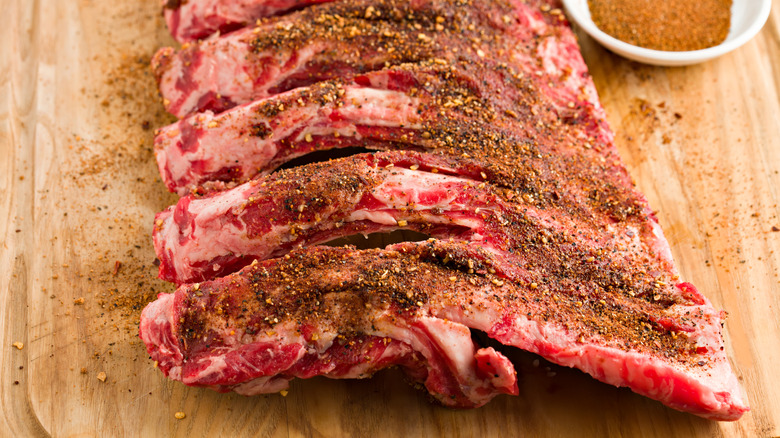 Dry rub on raw rack of ribs on cutting board.