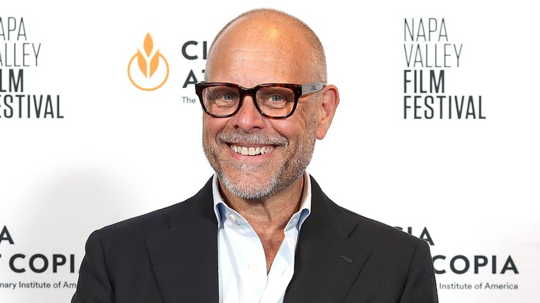 Alton brown smiling with teeth wearing dark-framed glasses