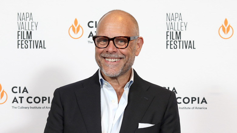 Alton Brown wearing a suit and smiling