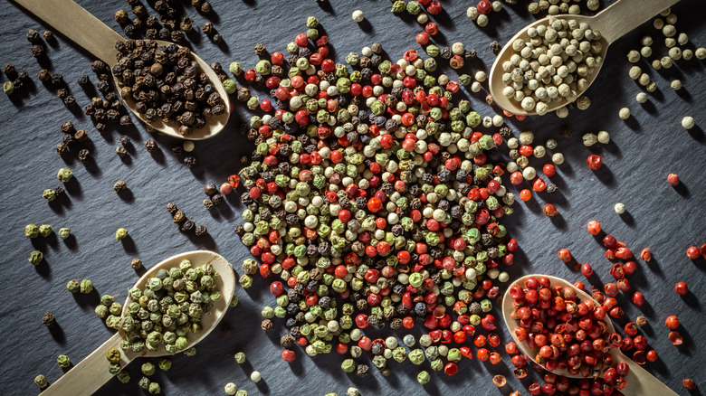 A variety of peppercorns on a black slate