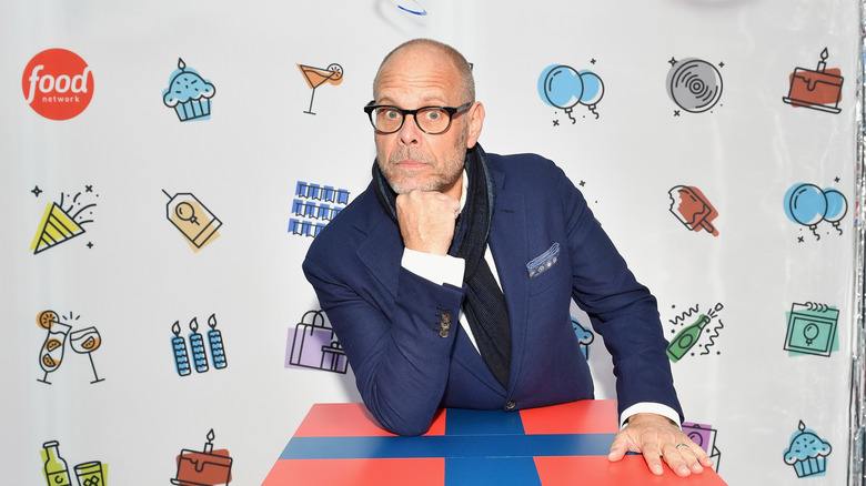 Alton Brown propped his head on his fist while leaning on a gift box