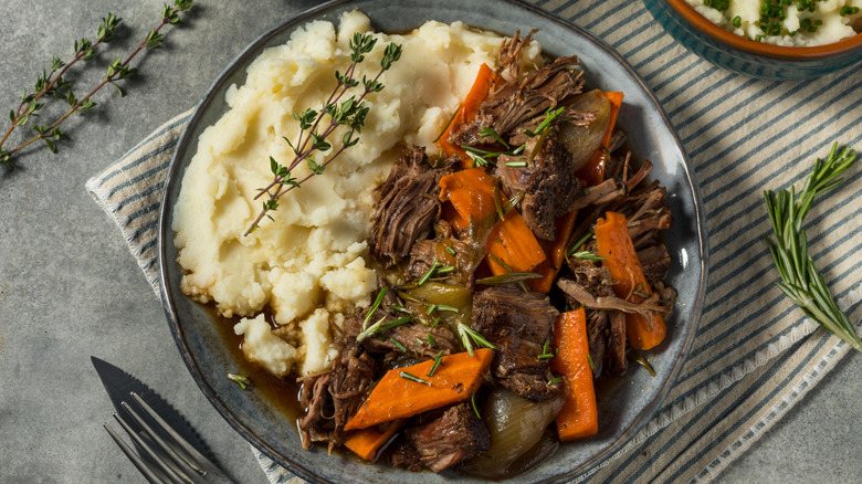 Pot roast with mashed potatoes, garnished with thyme on a ceramic plate