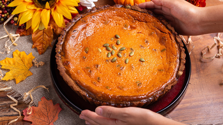 Pumpkin pie topped with pumpkin seeds surrounded with autumn decor