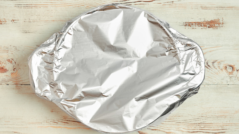 A container wrapped in aluminum foil against a rustic wooden background.
