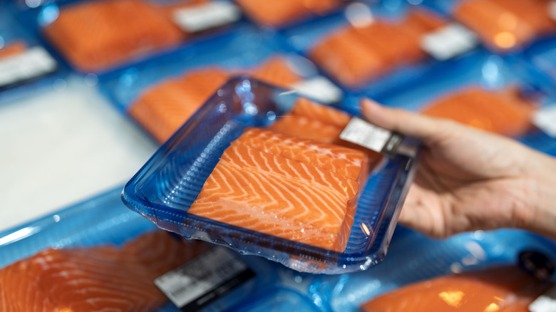 Hand holding a package of salmon fillets over other packages