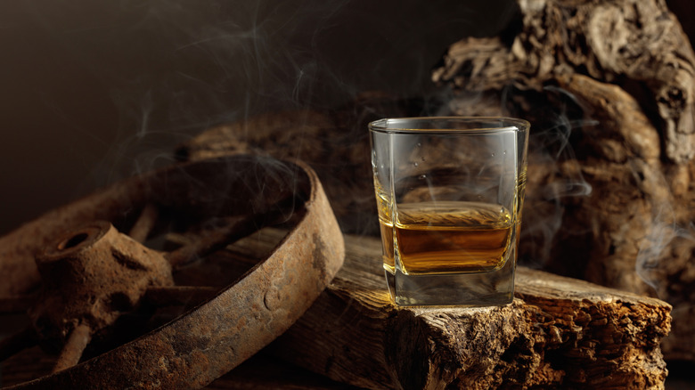 A glass of whiskey on a wooden board.