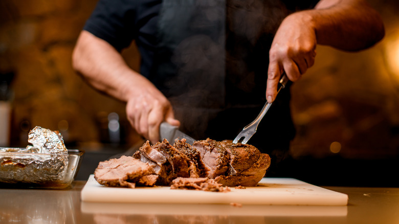 Chef wearing black shirt slicing cut of steak