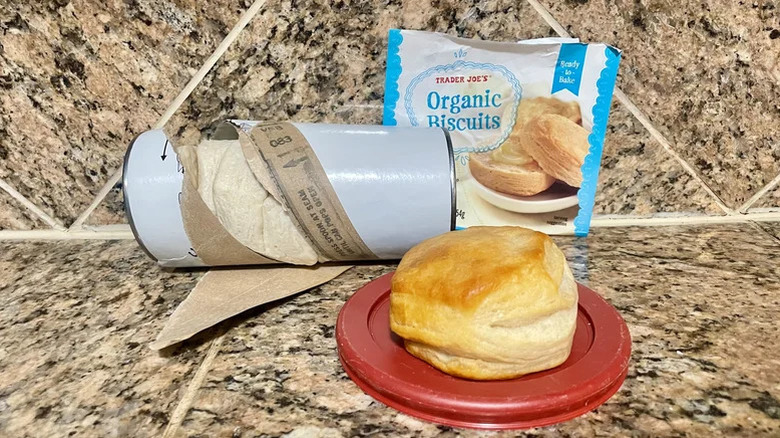 An opened can of Trader Joe's Organic Biscuits next to one single baked biscuit
