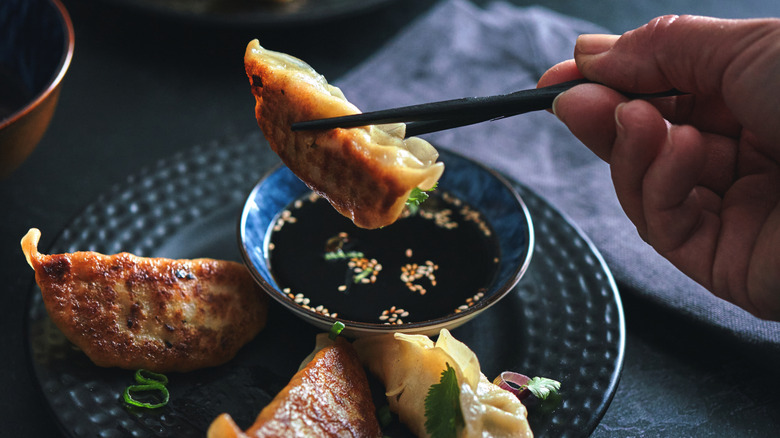 Person dipping gyoza into soy sauce with chopsticks.