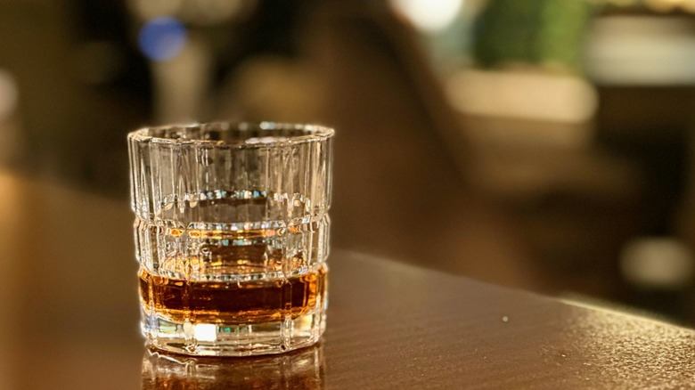A glass of bourbon served neat on top of a bar.